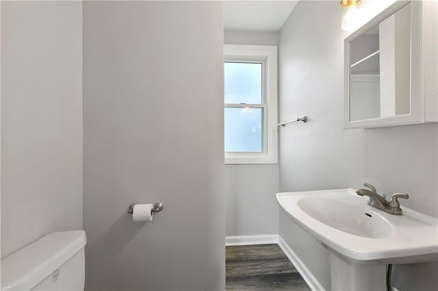 half bath featuring baseboards, wood finished floors, and toilet