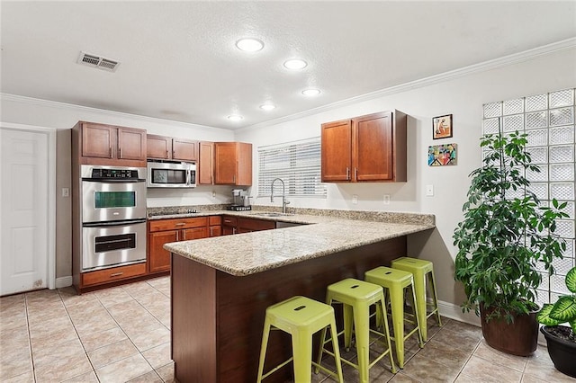 kitchen with a kitchen bar, a peninsula, visible vents, a sink, and stainless steel appliances