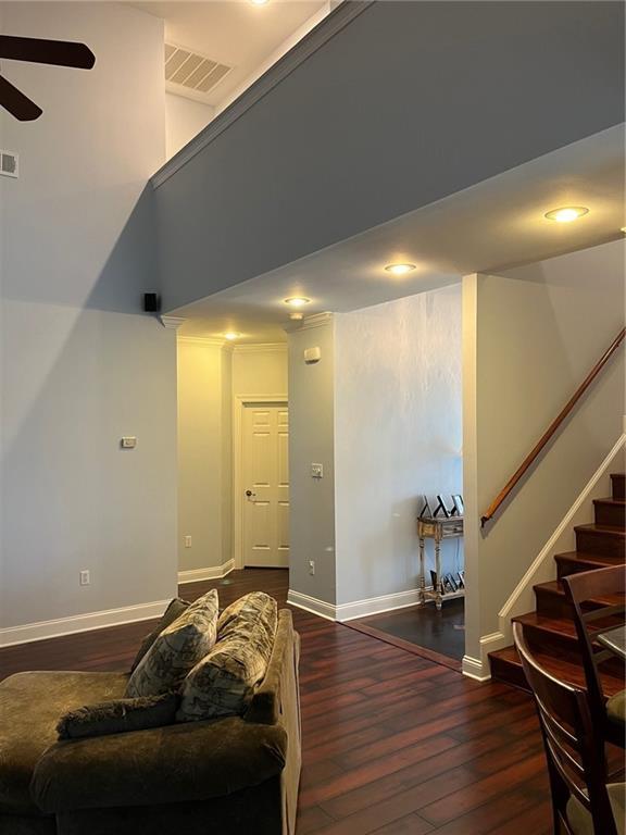 living area featuring visible vents, baseboards, ceiling fan, stairway, and wood-type flooring