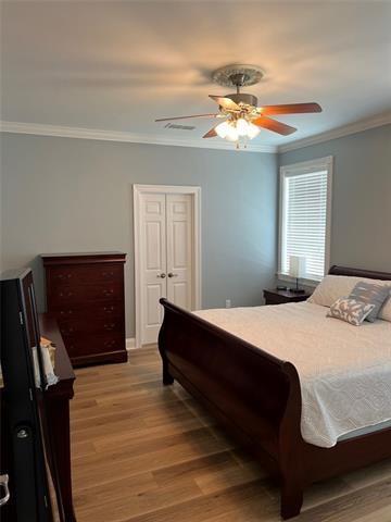bedroom featuring a closet, a ceiling fan, light wood finished floors, visible vents, and ornamental molding