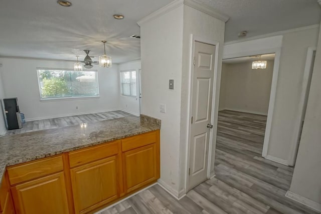7984 Edgelake Ct, New Orleans, LA 70126 - kitchen with an inviting chandelier, brown cabinetry, light wood-type flooring, stone counters, and baseboards