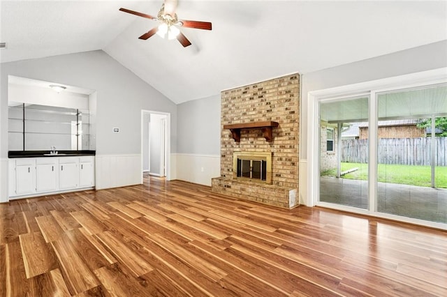 803 Lake Dcote Ct, Slidell, LA 70461 - unfurnished living room with light wood-style floors, ceiling fan, wainscoting, lofted ceiling, and a brick fireplace