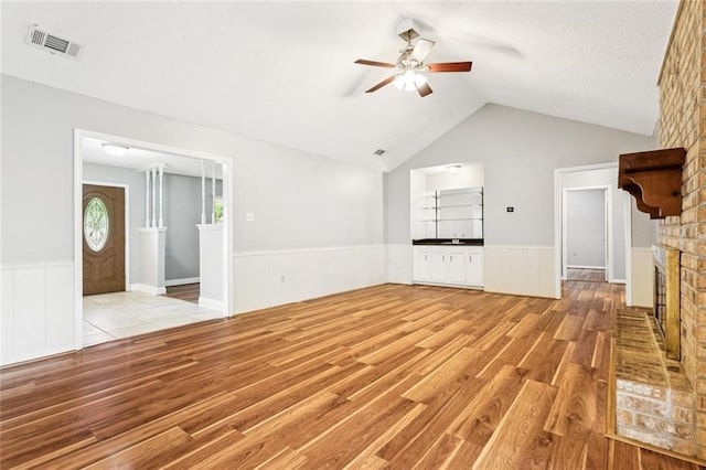 803 Lake Dcote Ct, Slidell, LA 70461 - unfurnished living room featuring a wainscoted wall, light wood-type flooring, a ceiling fan, a brick fireplace, and lofted ceiling