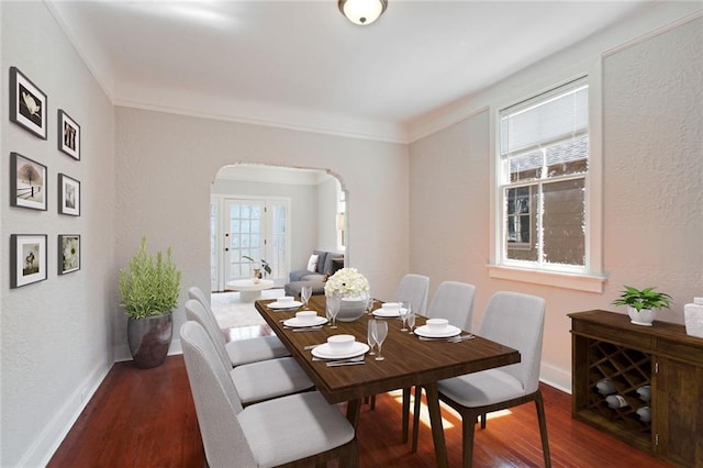dining space featuring arched walkways, baseboards, a healthy amount of sunlight, and wood finished floors