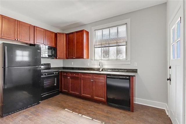 kitchen featuring dark wood-type flooring, baseboards, a sink, dark countertops, and black appliances