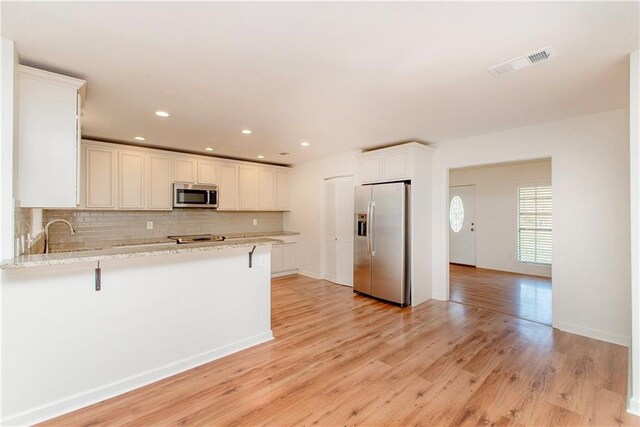 17168 E Little Italy Rd, Hammond, LA 70403 - kitchen with tasteful backsplash, light wood-type flooring, stainless steel appliances, visible vents, and a peninsula