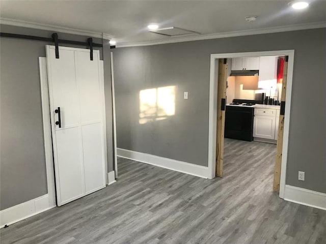 interior space with baseboards, a barn door, wood finished floors, and crown molding