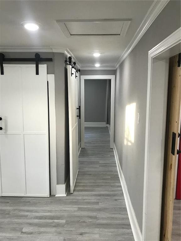 hallway with baseboards, a barn door, wood finished floors, and ornamental molding