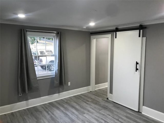 unfurnished bedroom with a barn door, ornamental molding, and wood finished floors