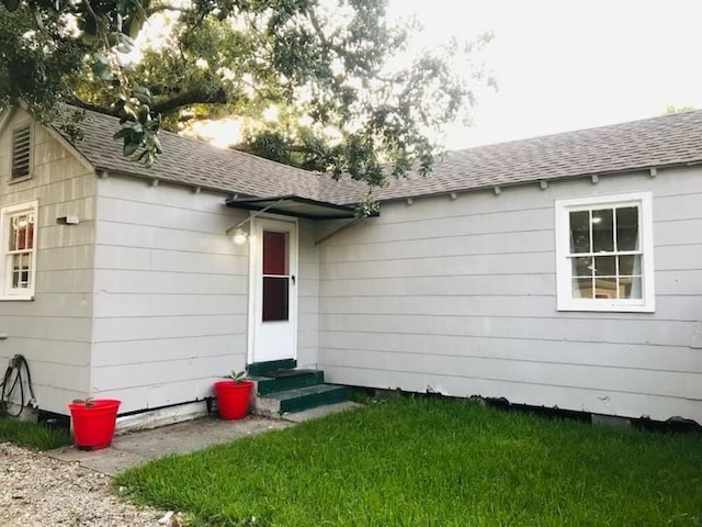 property entrance with a lawn and a shingled roof