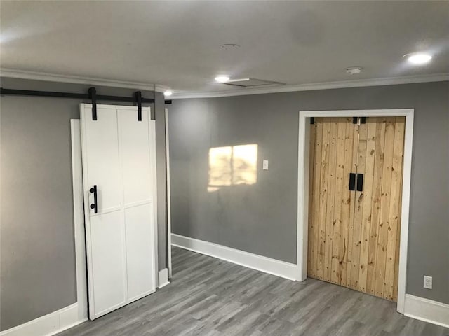 interior space with baseboards, a barn door, wood finished floors, and crown molding