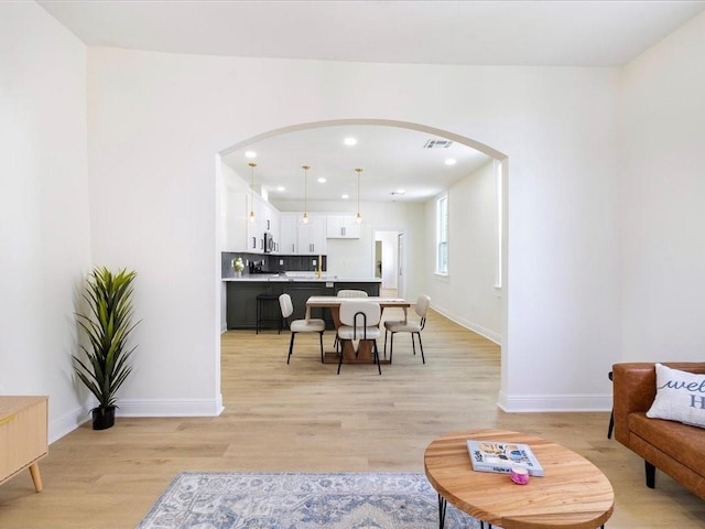 living room with light wood-style flooring, baseboards, visible vents, arched walkways, and recessed lighting