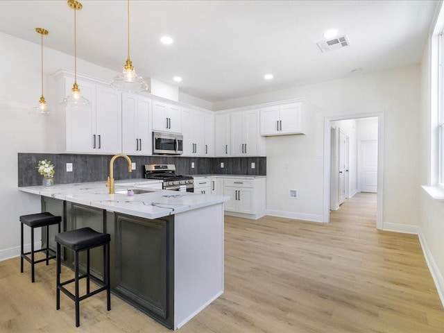 kitchen with white cabinets, a peninsula, light stone countertops, appliances with stainless steel finishes, and a sink