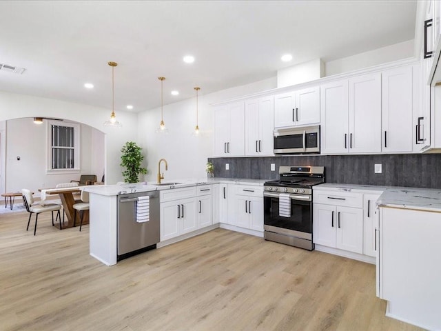 kitchen featuring a sink, arched walkways, visible vents, a peninsula, and appliances with stainless steel finishes