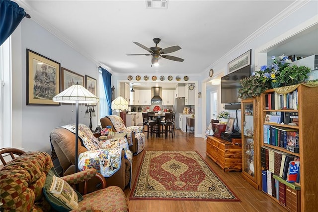 living room with dark wood-style flooring, visible vents, crown molding, and ceiling fan