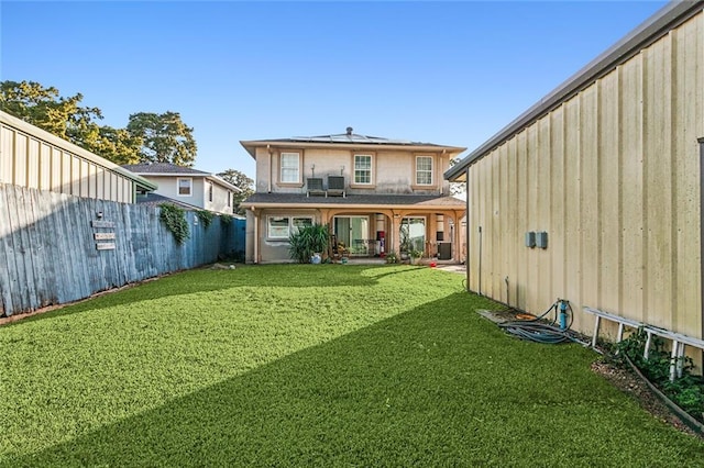 rear view of house featuring a lawn, fence, and solar panels