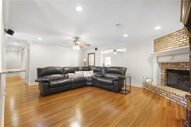 living area featuring crown molding, a fireplace, light wood-style flooring, visible vents, and ceiling fan