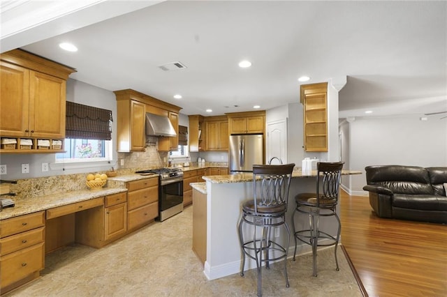 kitchen featuring visible vents, wall chimney exhaust hood, appliances with stainless steel finishes, open shelves, and a kitchen breakfast bar