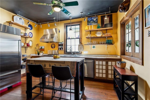 3342 Bell St, New Orleans, LA 70119 - kitchen featuring open shelves, stainless steel appliances, dark wood finished floors, wall chimney range hood, and a ceiling fan