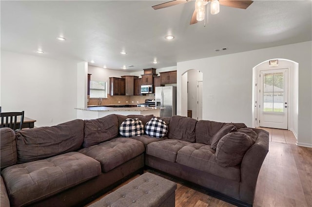 living room featuring light wood-type flooring, arched walkways, recessed lighting, and a ceiling fan