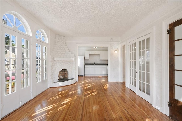 4237 Fontainebleau Dr, New Orleans, LA 70125 - unfurnished living room with french doors, a textured ceiling, hardwood / wood-style floors, and a stone fireplace
