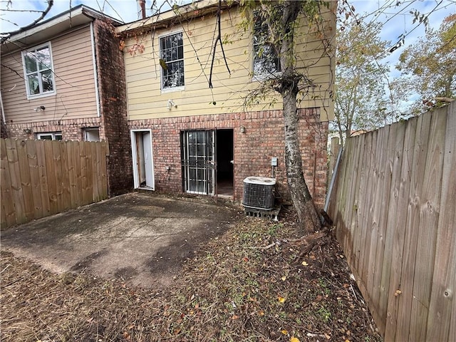 rear view of property with a fenced backyard, brick siding, a patio area, and central AC