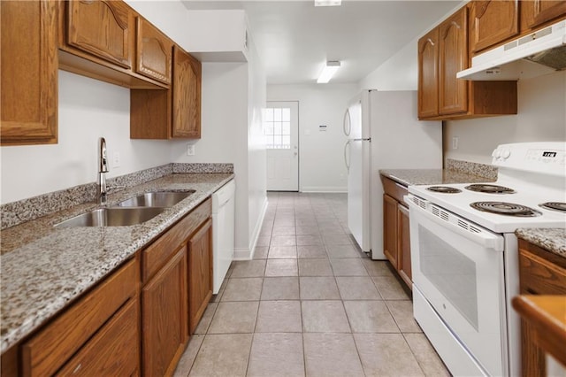 kitchen with light stone countertops, brown cabinets, a sink, under cabinet range hood, and white appliances