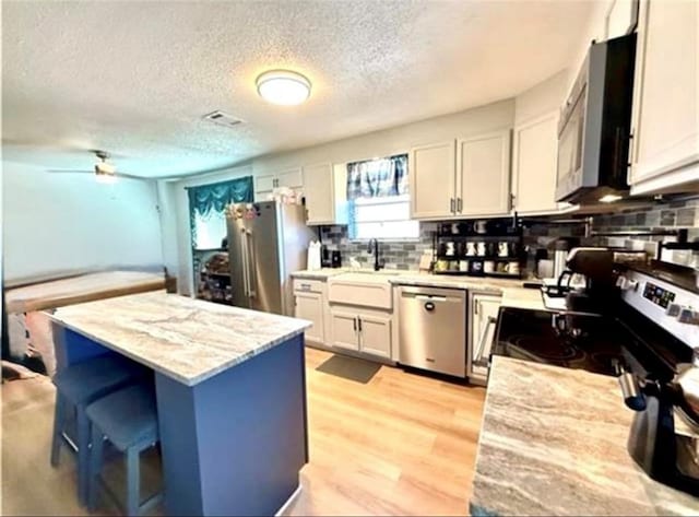2516 E Pearl Dr, Marrero, LA 70072 - kitchen featuring appliances with stainless steel finishes, a textured ceiling, backsplash, a kitchen island, and light wood-style flooring