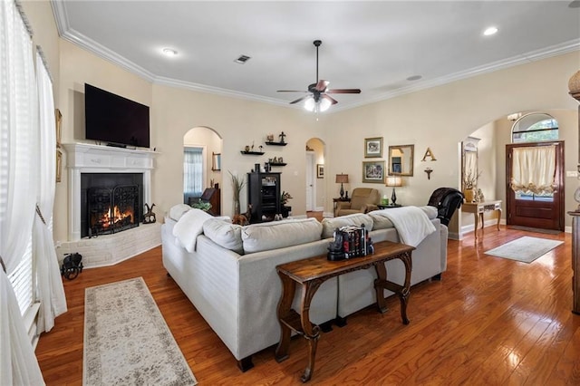 301 Clover Meadows Dr, Covington, LA 70433 - living room with arched walkways, a brick fireplace, wood finished floors, crown molding, and a ceiling fan