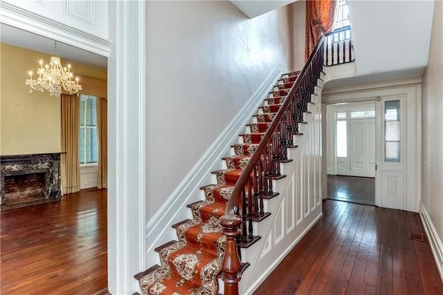 stairs with wood-type flooring, a towering ceiling, a chandelier, and a fireplace