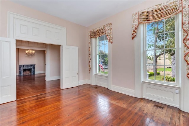 unfurnished room with hardwood / wood-style floors, a chandelier, a premium fireplace, baseboards, and visible vents