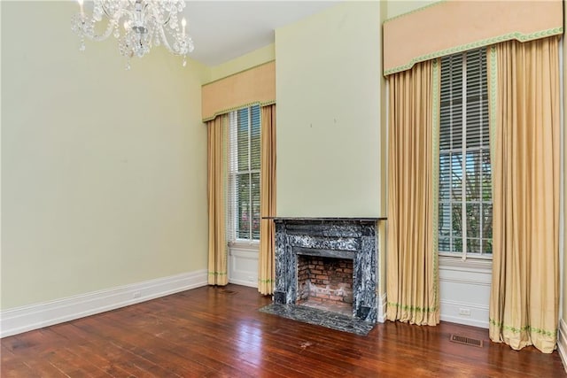 unfurnished living room featuring baseboards, visible vents, a notable chandelier, hardwood / wood-style floors, and a fireplace