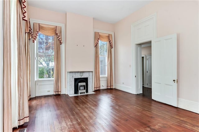 unfurnished living room featuring baseboards, a wood stove, dark wood-type flooring, and plenty of natural light