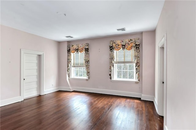 empty room featuring plenty of natural light, baseboards, visible vents, and dark wood finished floors