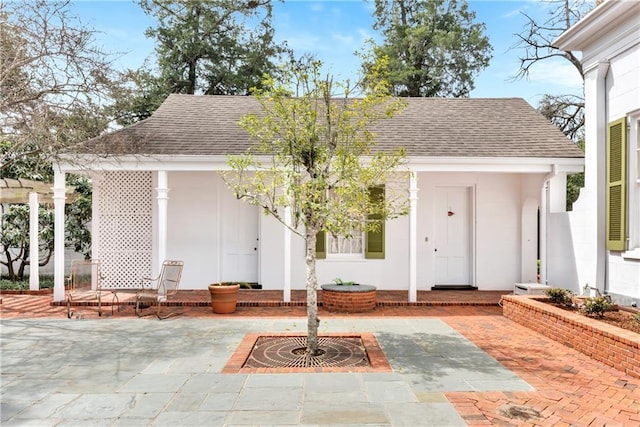 view of exterior entry with a patio area and roof with shingles