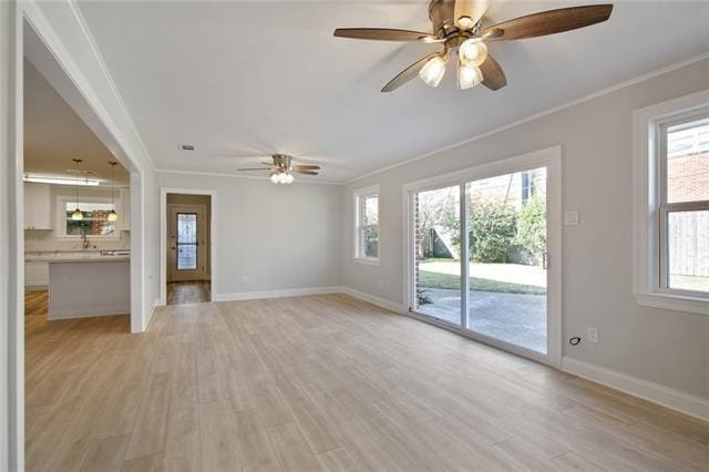 unfurnished living room with baseboards, ornamental molding, ceiling fan, and light wood-type flooring