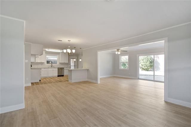 unfurnished living room featuring a sink, ceiling fan with notable chandelier, light wood-style flooring, baseboards, and ornamental molding