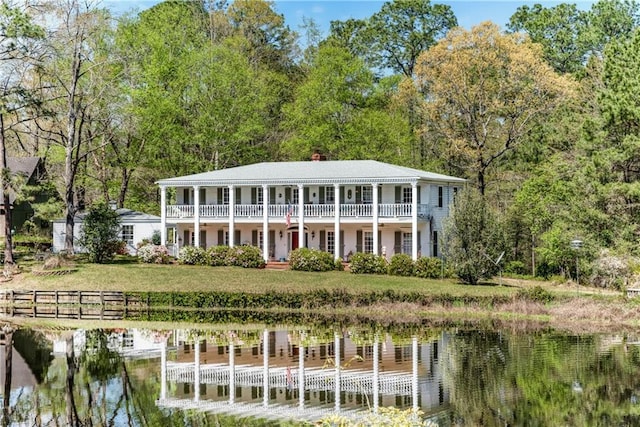 back of house with a chimney, a water view, a yard, and a balcony