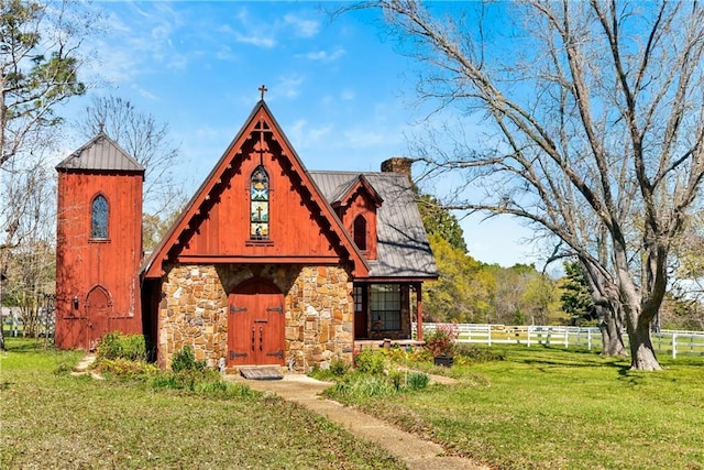 english style home with a chimney, a front lawn, stone siding, fence, and metal roof
