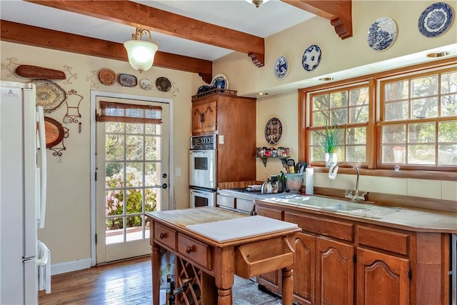 kitchen with double oven, wood finished floors, a sink, freestanding refrigerator, and beam ceiling
