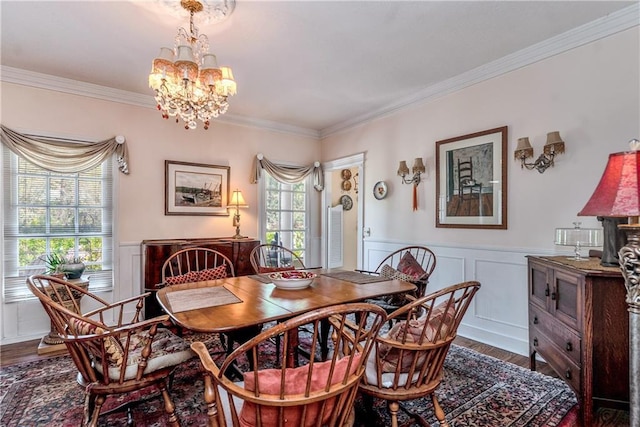dining room featuring wood finished floors, crown molding, a notable chandelier, and a wainscoted wall