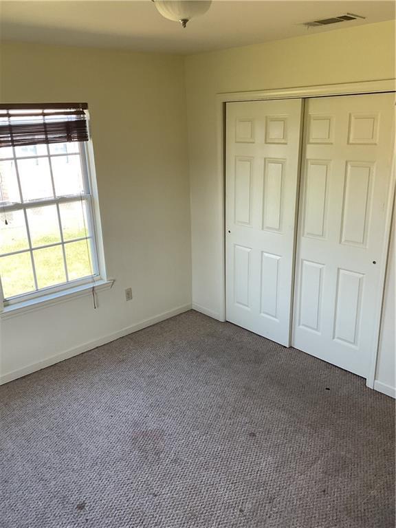 unfurnished bedroom featuring baseboards, a closet, dark colored carpet, and visible vents