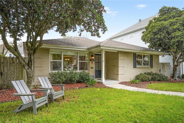 single story home with brick siding, fence, a shingled roof, and a front yard