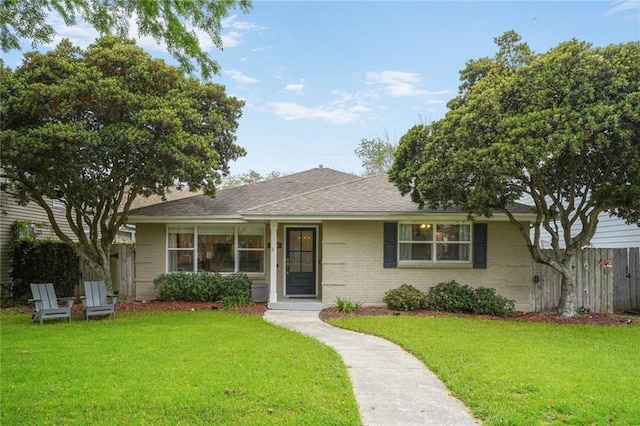 single story home with brick siding, fence, roof with shingles, and a front yard