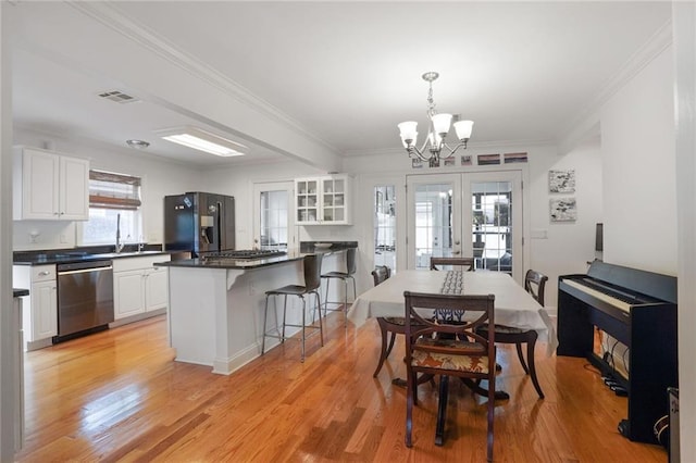 dining space with french doors, light wood finished floors, visible vents, ornamental molding, and an inviting chandelier