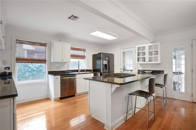 kitchen with a kitchen breakfast bar, dark countertops, stainless steel appliances, visible vents, and white cabinets