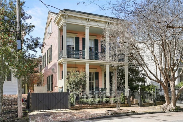 greek revival inspired property with a balcony, covered porch, a fenced front yard, and a gate