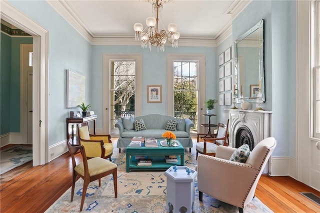 living area with crown molding, baseboards, a chandelier, visible vents, and wood finished floors