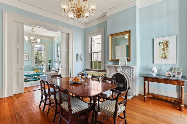 dining space featuring an inviting chandelier, ornamental molding, hardwood / wood-style flooring, and a fireplace