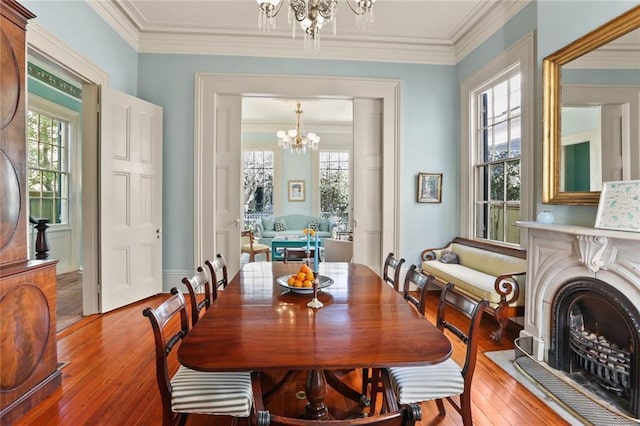 dining room with wood-type flooring, crown molding, a fireplace, and an inviting chandelier